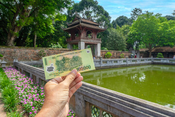 Vietnam dong bank note in woman hand on fortress of Van Mieu background. The money contains a pict of the ancient Vietnamese fortress of Van Mieu (Temple Of Literature) , Hanoi, Vietnam