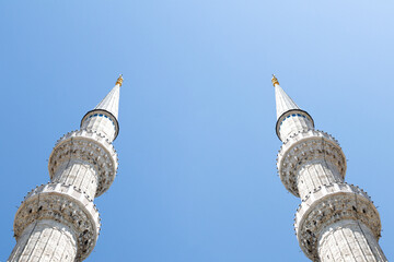 Two minarets isolated on blue sky background. Minaret is the place where the call to prayer is recited in mosques. Place of worship. Copy space, blank, empty. No people, nobody. Religion, belief. 
