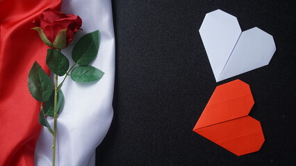 Crumpled red and white Indonesian flag with a rose and two heart shaped origami isolated on black background