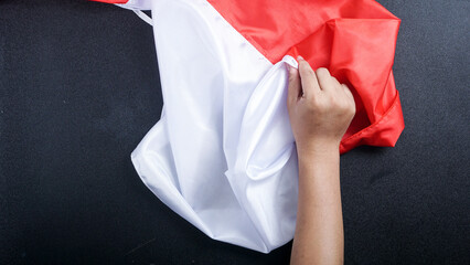 A hand holding red and white flag of Indonesia to celebrate Indonesia independence day isolated on black background