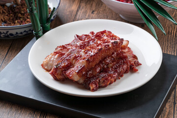 Honey-glazed barbecued pork in a rice-colored porcelain plate is placed on a camphorwood cutting board