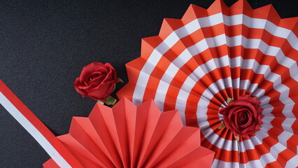 Independence Day Indonesia banner mockup with a rose, Indonesia flag color paper fans, and ribbons isolated on black background