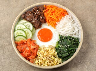 Bibimbap is a Korean dish in the form of a bowl of white rice topped with side dishes of vegetables, beef, eggs and spicy gochujang sauce.