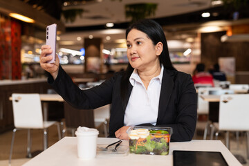 businesswoman in restaurant having coffee and salad while taking selfie