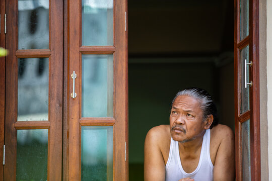 Elderly man leaning at window, deep in thought and quiet reflection