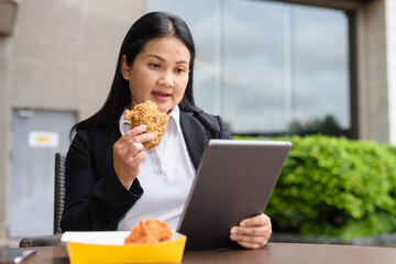 Businesswoman outdoors eating fried chicken and using tablet computer