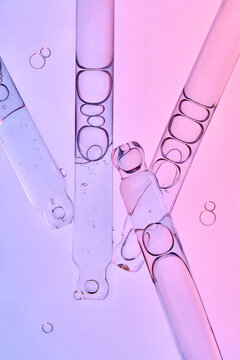 Several glass pipettes with liquid on gradient blue purple backdrop.