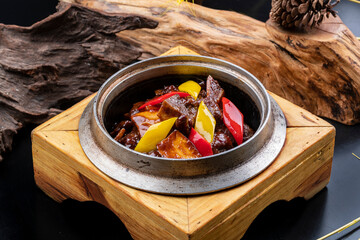 Sauteed beef ribs in a wooden iron pot placed on a black background