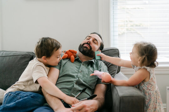 sleeping dad with his little boy on the sofa, sister is on the side