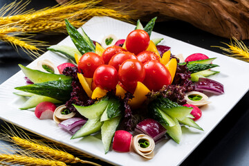 A square porcelain plate of mixed garden vegetables is placed on a black background