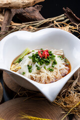 A heart-shaped porcelain bowl of Jin-style chicken soup noodles is placed on a camphorwood chopping board.
