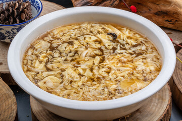 Hot and sour soup in a round soup bowl placed on a wooden board