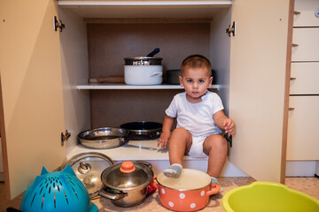 Curious toddler exploring kitchen cabinet and playing with pots and pans