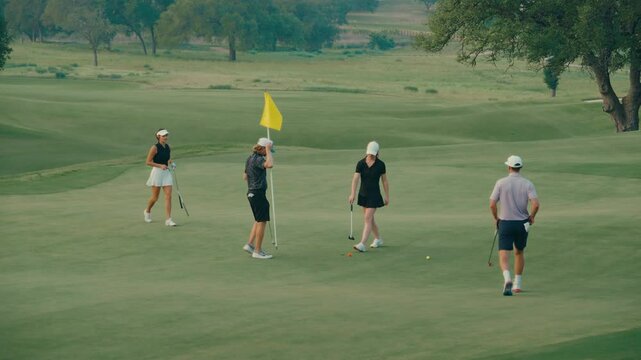 Golf foursome finishes their round on the 18th green. They putt, pull the flagstick, shake hands, and smile as they walk off together &mdash; a classic, sportsmanlike end to the round.
