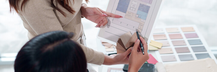 Asian women interior designers collaborate on blueprint with wood samples and color palettes for...
