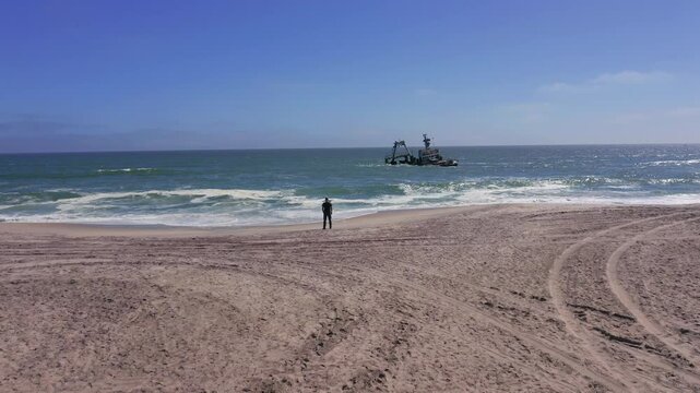 A man standing near beach shore overlooking Zeila Shipwreck, south Atlantic Ocean, Aerial tracking shot
