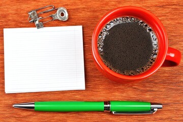 Red mug of coffee, notepad, and pen on a wooden table