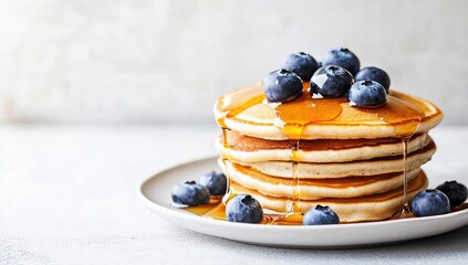 Stack of fluffy pancakes drizzled with honey, topped with blueberries