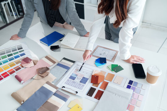 Interior Design Meeting: Asian Women Architects Reviewing Blueprints, Color Swatches and Fabric Samples for Home Renovation and Creative Interior Decor Projects
