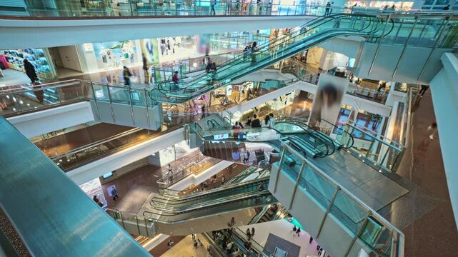 Bright Multi-Level Shopping Mall Interior Revealing Escalators Transporting Shoppers Between Floors. Very Busy Full of Clients Shopping Mall Interior With Escalators And Customers. Time Lapse