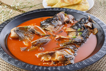 Black iron plate with thick soup and fish head in pancake