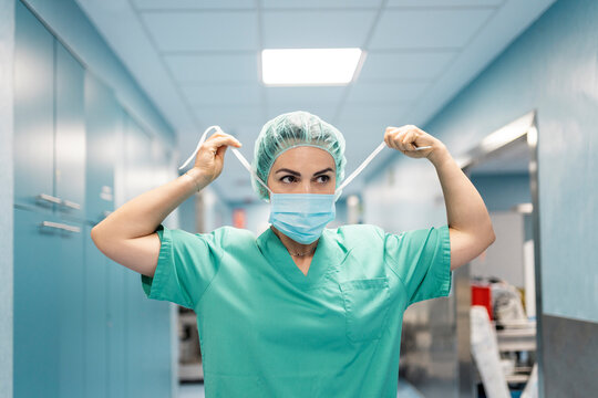 Female surgeon putting on surgical mask in hospital corridor