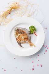 French grilled silver pomfret on a white porcelain plate