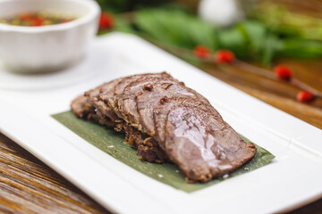 Beef tenderloin with dipping sauce on a rectangular white porcelain plate