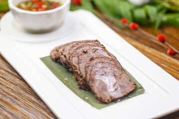 Beef tenderloin with dipping sauce on a rectangular white porcelain plate
