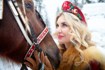 Beautiful Russian woman in national dress enjoys Maslenitsa holiday with a horse in winter scenery