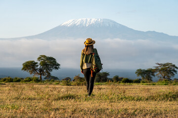 Stylish hipster girl in hat walking against the backdrop of peak of Kilimanjaro. Happy young woman...