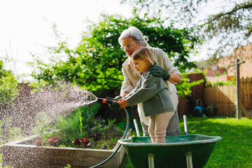 Grandmother and granddaughter watering plants in backyard garden