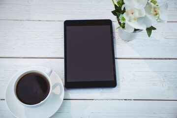 Flat design tablet is lying on white wooden plank table, showing coffee cup and potted plant