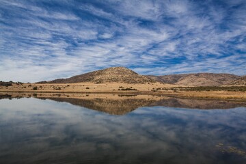Lake is reflecting solitary rounded hill under calm streaked clouds in flat design