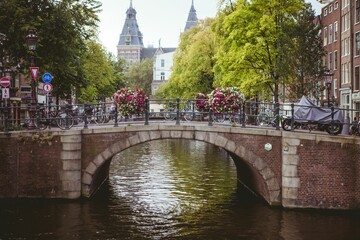 Stone arch canal bridge is spanning canal in flat style, with bicycles and hanging flower baskets