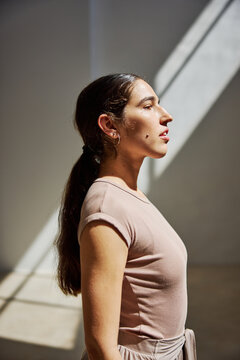 Woman standing in profile with sunlight casting shadows indoors