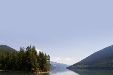 Trees at lakeshore by mountains against sky