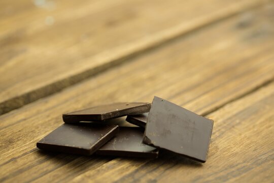 Naklejki Dark chocolate squares are overlapping on rustic wooden tabletop in 3D render with crumbs