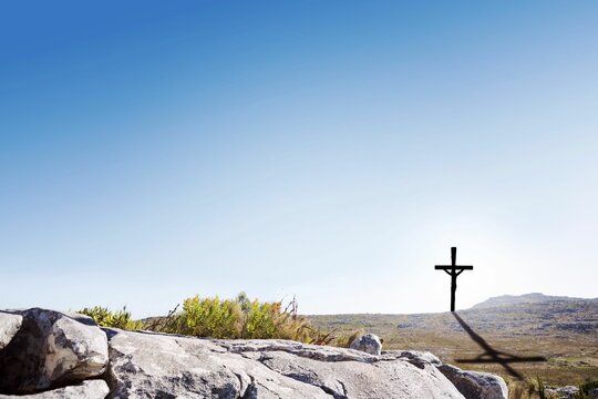 Fototapeta Showing flat design wooden cross standing on rocky hilltop, casting long shadow over green shrubs
