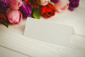 folded white place card is sitting on whitewashed tabletop, showing colorful tulip bouquet backdrop