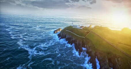 White lighthouse is standing on coastal cliff in flat design with sunlight and crashing waves