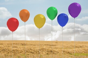 Six colorful balloons are floating in flat design over golden wheat stubble under pale blue sky
