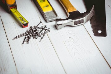 Flat design is showing tape measure, nails, spirit level, hammer, saw blade on white painted plank