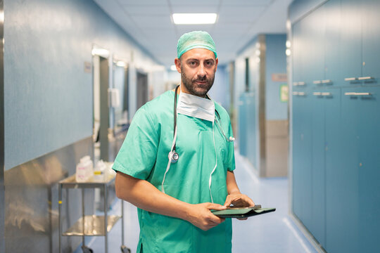 Confident surgeon using digital tablet in hospital corridor