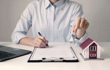 A female real estate agent holds a house key and explains the terms and conditions of the contract, details of renting and buying a house to the customer before signing the contract
