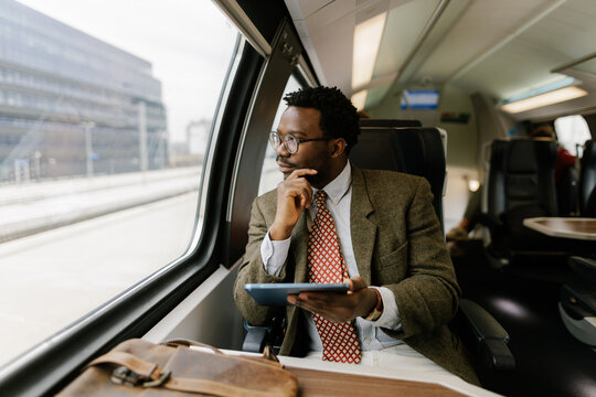Man Sitting Inside Train Observing Outside View While Using Tablet