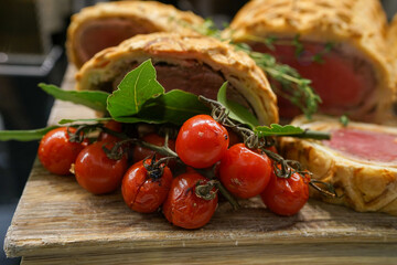 Roasted cherry tomato on the vine in front of slices of beef Wellington 