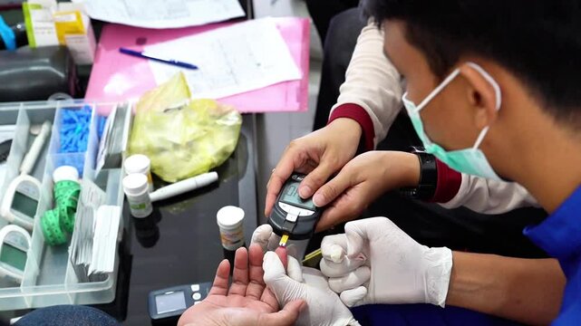 A medical professional checks a man's blood sugar level using a glucometer and test strip during a public health screening with diagnostic tools on the table