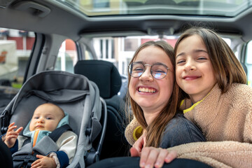 Sisters hugging in car. Baby in car seat. Happy family moment.