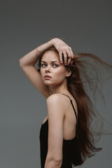 Naklejka premium young woman posing with long flowing hair and light skin, wearing a black dress with thin straps against a simple grey background in studio lighting